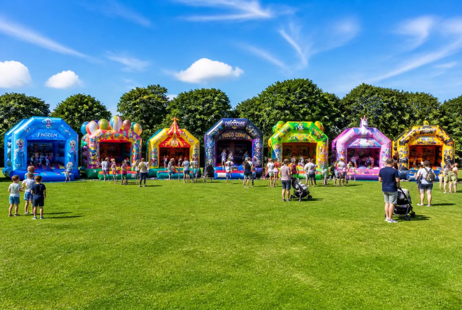Sieben bunte Hüpfburgen von Sprung & Süß Verleih nebeneinander auf einer Wiese bei einem Familienevent